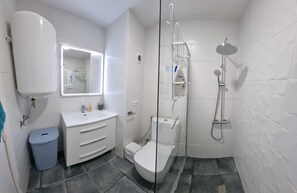 A modern bathroom with a white sink, mirror, toilet, and shower.