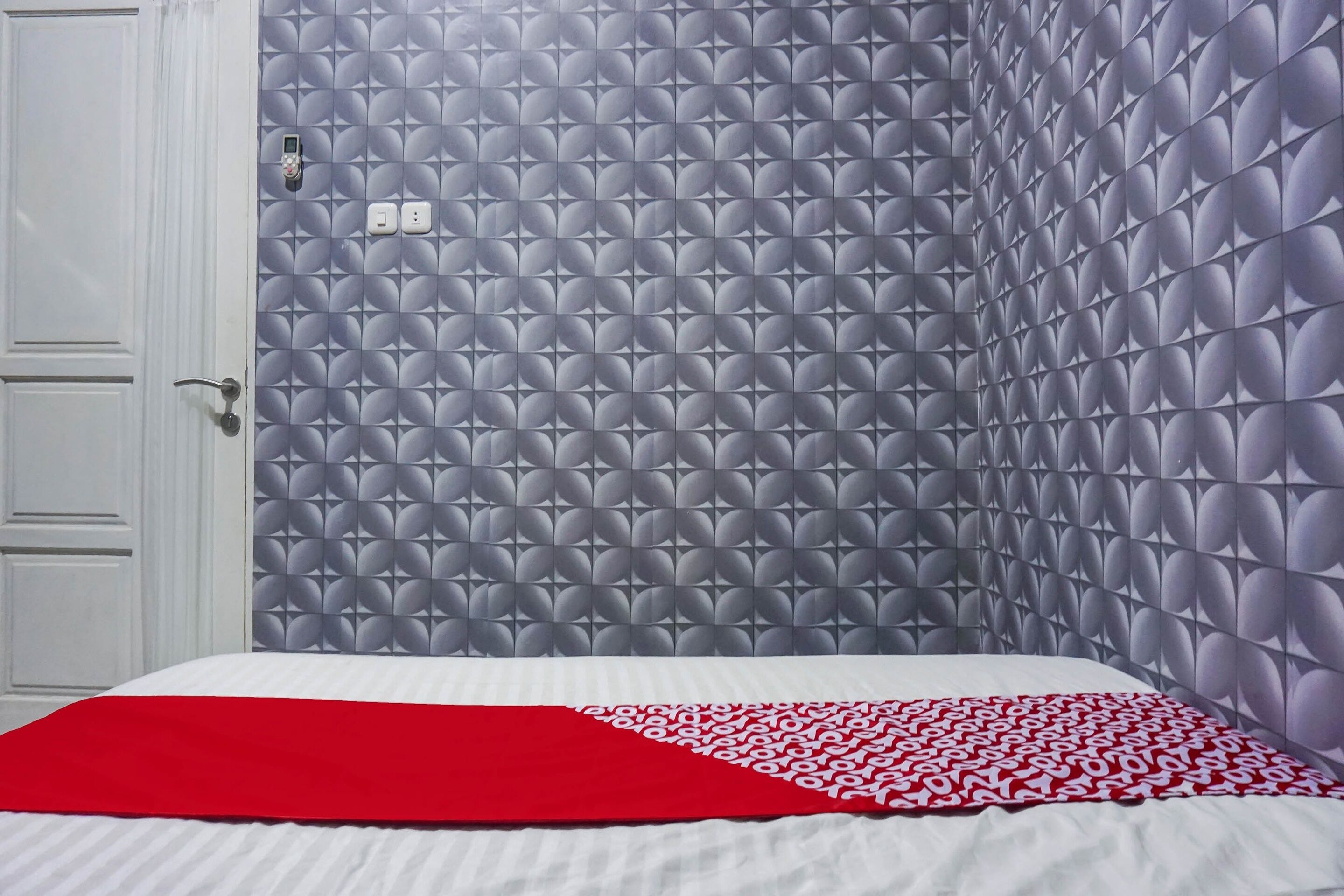 Ein Zimmer mit einem Bett, einer rot-weißen Bettdecke und einer Wand mit geometrischem Muster.