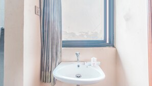 Un baño con un lavamanos blanco, una ventana con vista a edificios y una cortina.