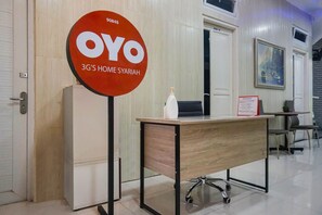 Un comptoir d’accueil avec une pancarte indiquant « OYO 3G’S HOME SYARIAH » et une petite table sur laquelle se trouvent une bouteille et une autre pancarte.