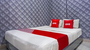 Una habitación de hotel con papel tapiz estampado, una cama con ropa blanca y detalles rojos, y dos almohadas con el nombre de marca 'OYO'.