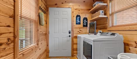 A compact laundry room with wooden walls, a white door, and a washing machine.