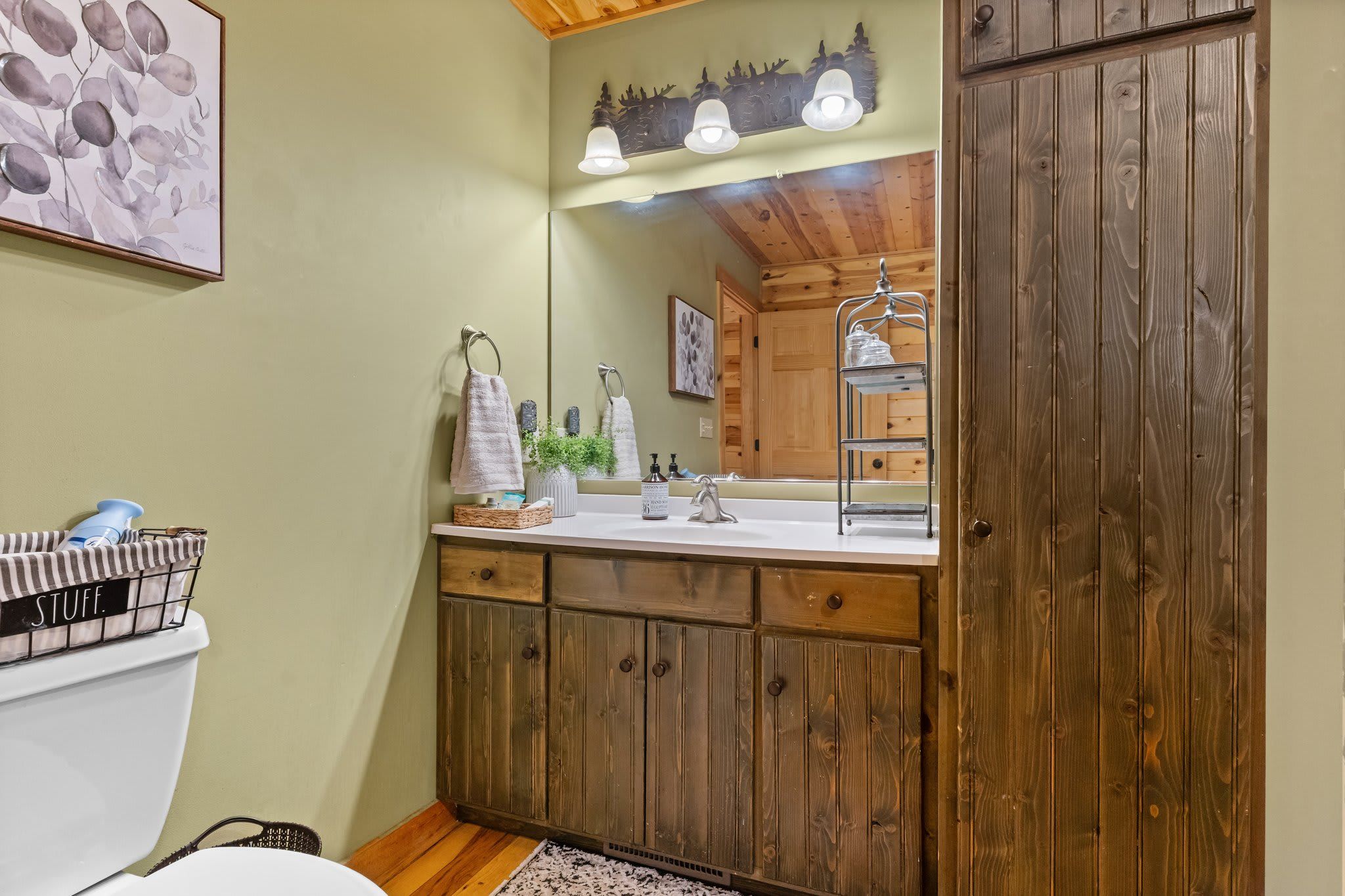 A bathroom with wooden cabinets, a sink with a mirror, and a framed artwork on the wall.