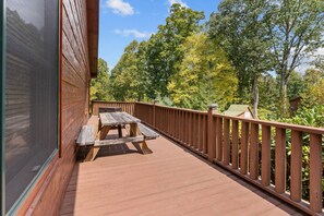 Een houten terras met een picknicktafel, omringd door een houten balustrade en bomen.