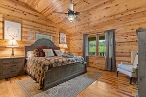 Een slaapkamer in een houten chalet met een bed, nachtkastjes, een stoel en een plafondventilator.