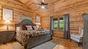Une chambre dans une cabane en bois, avec un lit, des tables de chevet, une chaise et un ventilateur de plafond.