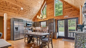 Une cuisine spacieuse aux murs en bois, une grande table à manger et une vue sur l’extérieur.