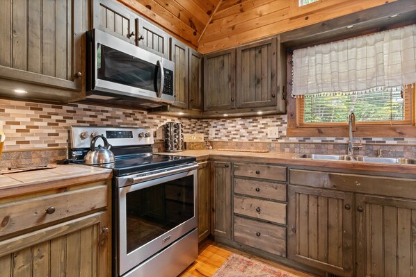 A kitchen with wooden cabinets, a stainless steel stove, a microwave, and a window with a white valance.
