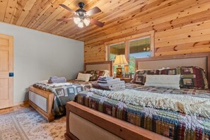 Een slaapkamer in een houten hutje met twee bedden, een plafondventilator en een raam met jaloezieën.