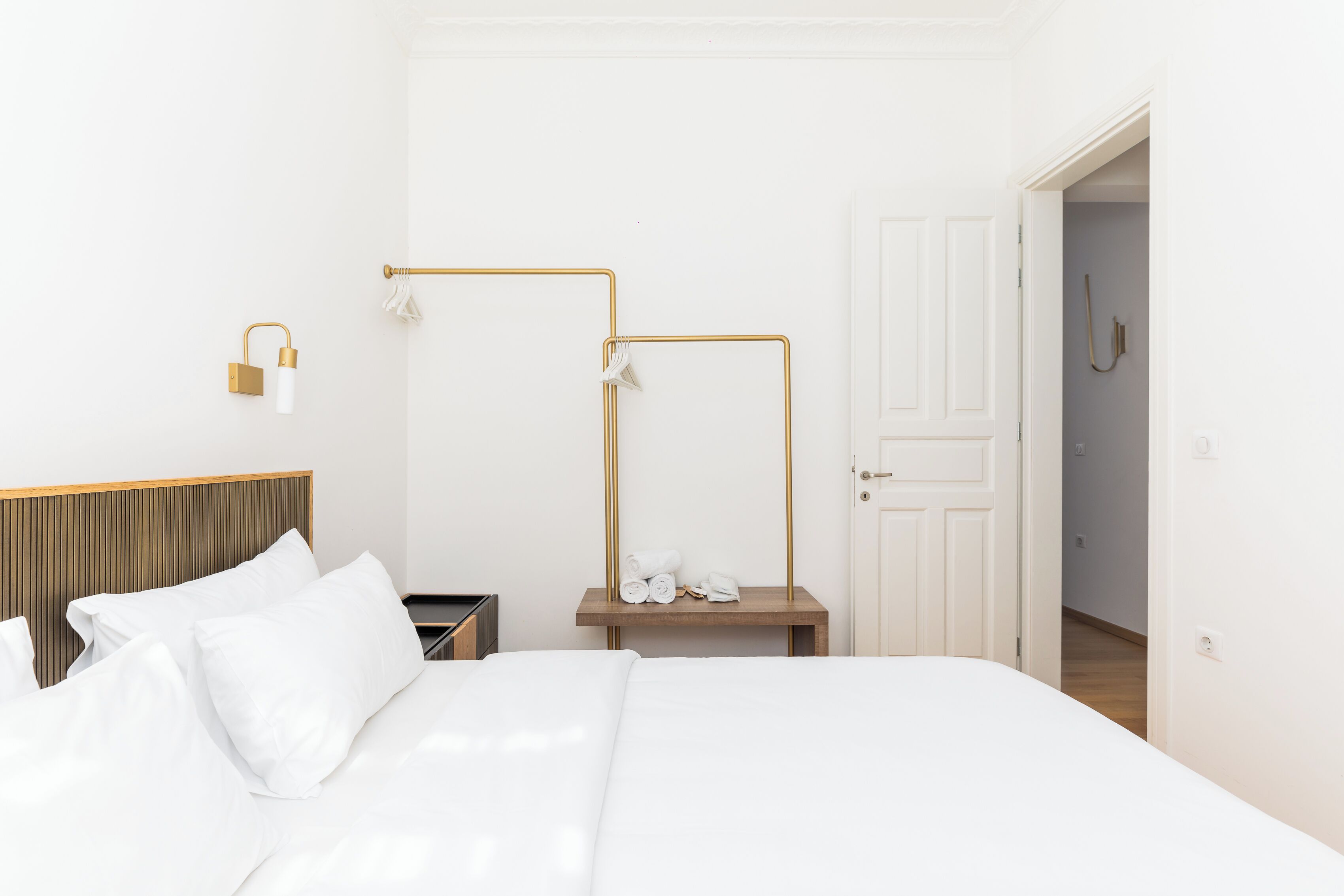 A neatly made bed with white linens, a wooden headboard, and a bedside table with a lamp and towels.