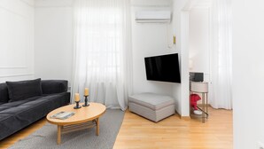 A modern living room with a sofa, a coffee table, a TV mounted on the wall, and a small side table. - Zoe by halu (Thessaloniki)