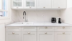 A modern kitchen with white cabinets, a marble countertop, a sink, and a coffee maker. - Zoe by halu (Thessaloniki)