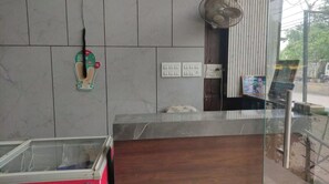 Un espace d’accueil avec un mur en marbre, un comptoir en verre, un ventilateur et une photo encadrée accrochée au mur.