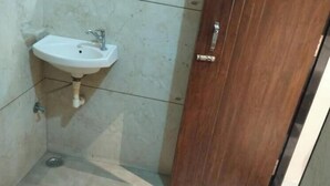 Ένα μπάνιο με έναν λευκό νιπτήρα, μια ξύλινη πόρτα και ένα κόκκινο κουβά στο πάτωμα.