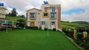 A two-story building with a flat roof, a small balcony, and a window with a yellow frame. - Rose garden enclave for families  (Ooty)