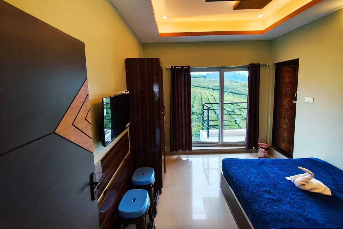 A hotel room with a bed, a TV, a desk, and a window with a view of a green landscape.