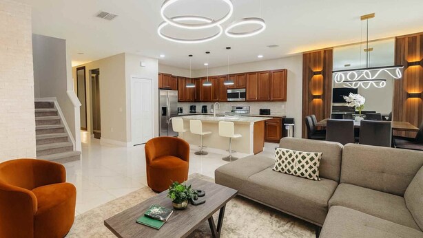 A modern living room with a sofa, two armchairs, a coffee table, and a kitchen in the background. - 4555 Amazing House W/Pool near Disney world (Kissimmee)