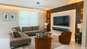 A modern living room with a sofa, two armchairs, a coffee table, and a flat-screen TV mounted on the wall. - 4555 Amazing House W/Pool near Disney world (Kissimmee)