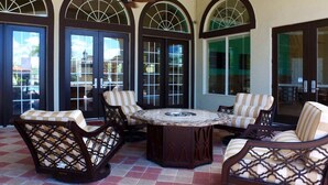 A covered patio area with a round table surrounded by striped cushioned chairs, large arched windows, and a view of the surrounding buildings. - 4555 Amazing House W/Pool near Disney world (Kissimmee)