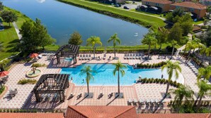 A large outdoor swimming pool with lounge chairs and a pergola, surrounded by palm trees and a view of a lake. - 4555 Amazing House W/Pool near Disney world (Kissimmee)