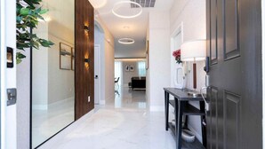 A modern hallway with a glass door, a wooden panel wall, and a console table with a lamp. - 4555 Amazing House W/Pool near Disney world (Kissimmee)