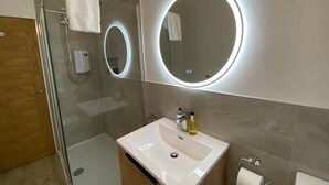Ein modernes Badezimmer mit einer Duschkabine aus Glas, einem weißen Waschbecken mit Spiegel darüber und einer Toilette.