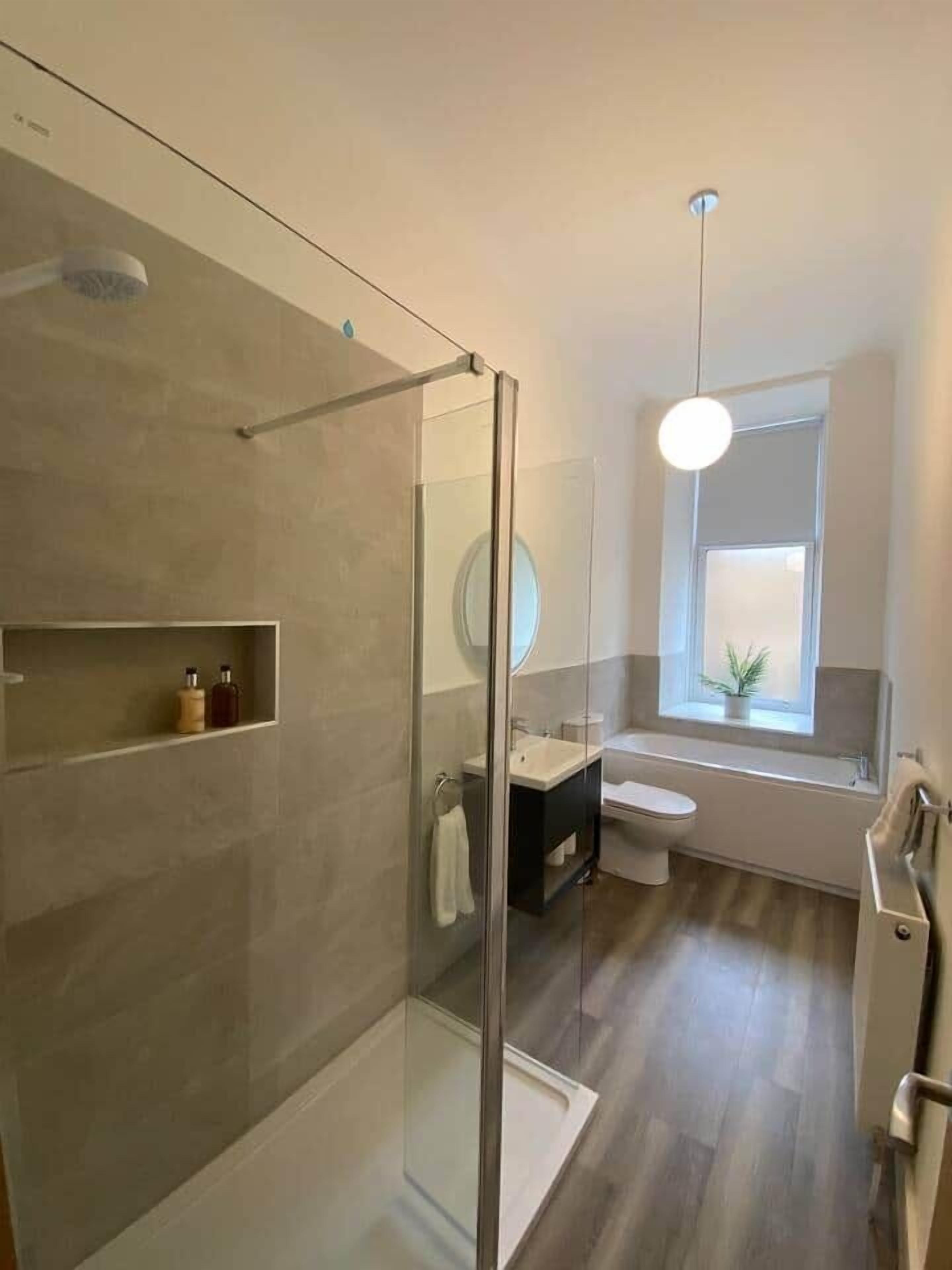 A modern bathroom with a glass shower enclosure, a sink, a toilet, and a window providing natural light.