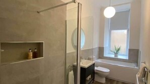 Een moderne badkamer met een douchecabine van glas, een wastafel, toilet en een raam voor natuurlijk licht.