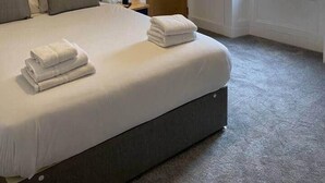 Een netjes opgemaakt bed met opgevouwen handdoeken, een bedlampje en een raam met uitzicht op gebouwen.