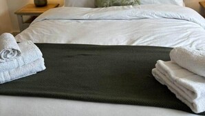 Un lit bien fait, avec des draps blancs, un coussin vert et des serviettes pliées posées sur le lit.