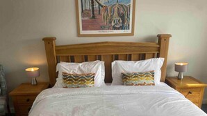 Una cama bien hecha con sábanas blancas y almohadas estampadas, un cabecero de madera y dos mesitas de noche con lámparas.