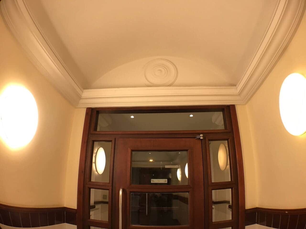 L’entrée d’un hôtel, avec une porte en bois, des panneaux de verre et deux appliques murales.