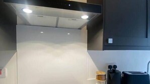 Una cocina moderna con una placa de inducción negra, una campana extractora de acero inoxidable y armarios oscuros.