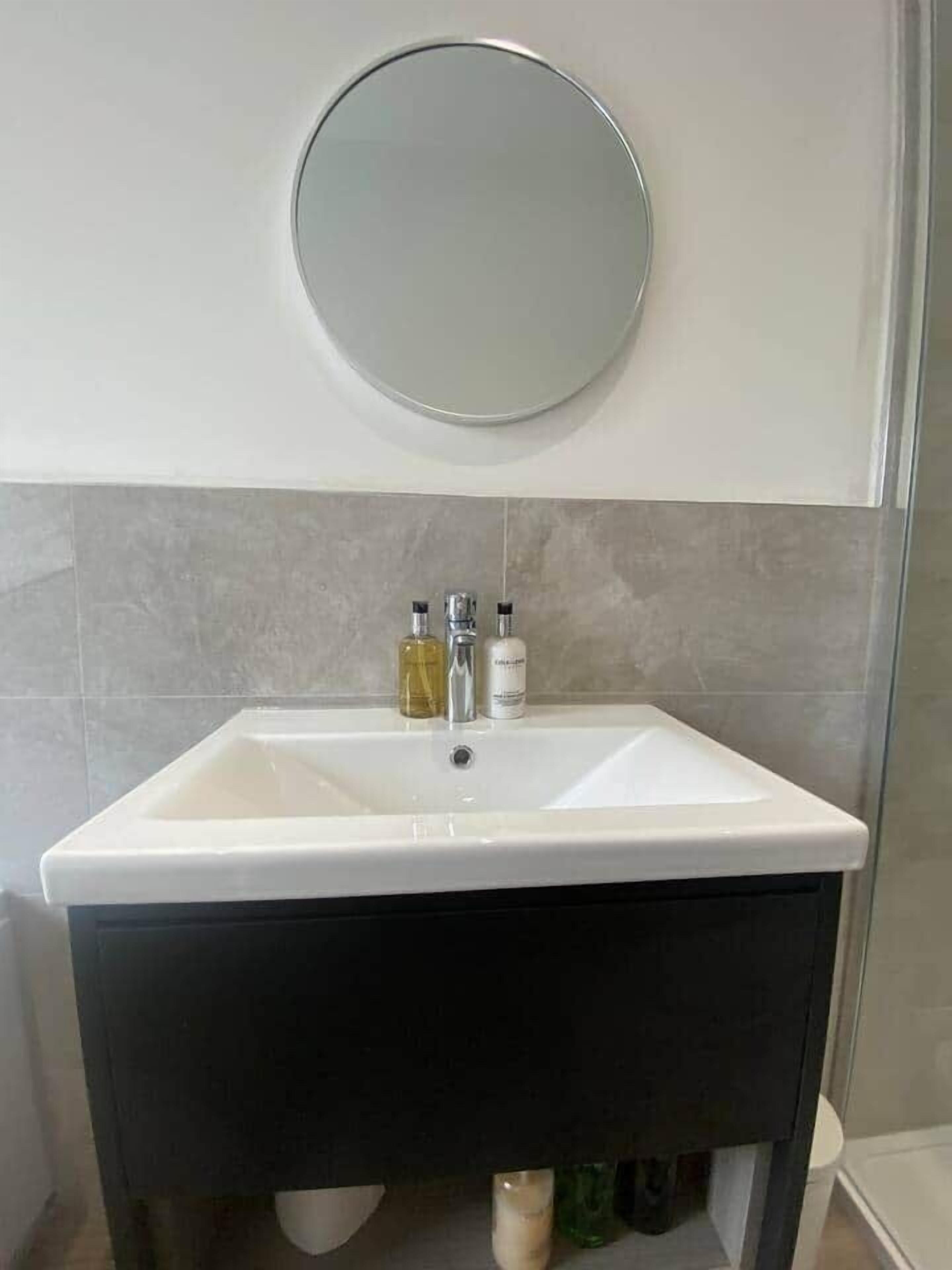 A bathroom with a white sink, two bottles of liquid soap, and a round mirror above the sink.