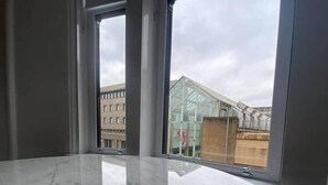 Una habitación con una amplia y brillante mesa de mármol, grandes ventanales que ofrecen vistas a edificios y un invernadero.