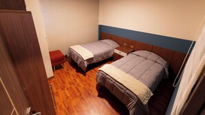 Habitació amb dos llits individuals, un sòl de fusta, una panxa vermella i un armari de fusta.
