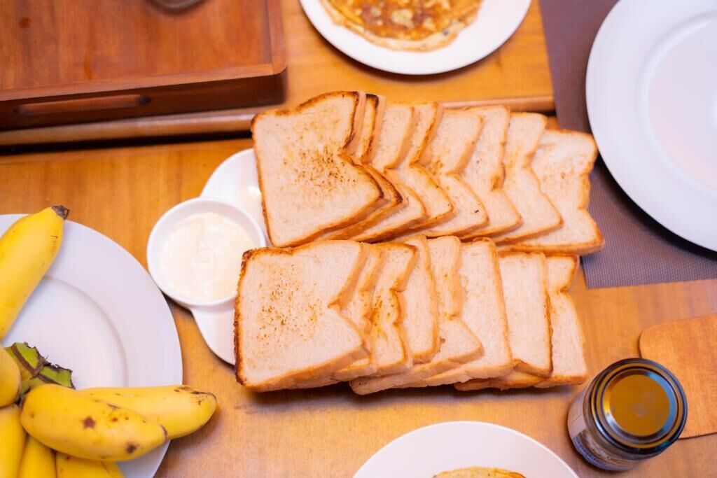 A table with sliced white bread, a plate of bananas, a small bowl of butter, and a glass of honey.