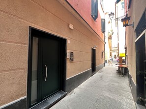 A narrow alleyway with a black door and a small window on a textured wall. - GOLD APARTMENT (Rapallo)