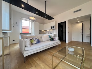 A modern living room with a sofa, a glass coffee table, and a kitchen in the background. - GOLD APARTMENT (Rapallo)