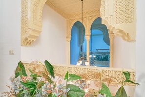 An ornate interior with detailed arches and a balcony with lush plants.