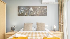 A hotel room with a checkered bedspread, two pillows, a cityscape artwork on the wall, a bedside lamp, and a window with curtains. - Holiday Home 'Casa Ramos Con Jacuzzi' with Sea View, Wi-Fi and Air Conditioning (Nerja)