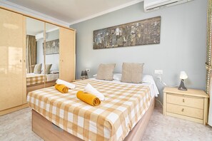 A hotel room with a checkered bedspread, a cityscape painting, a wardrobe, a bedside table with a lamp, and a mirror. - Holiday Home 'Casa Ramos Con Jacuzzi' with Sea View, Wi-Fi and Air Conditioning (Nerja)