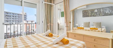 Une chambre d’hôtel avec une couvre-lit à carreaux, un grand miroir, une vue sur la ville et un balcon avec des rideaux.