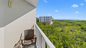 A balcony with a chair, overlooking a building and a coastal landscape.