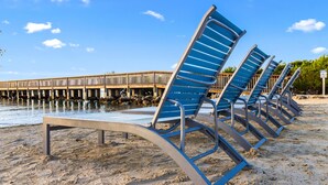 A row of blue beach chairs on a sandy beach with a wooden pier in the background. - Family-Friendly 1BR w/ Partial Ocean View & Pool (Tavernier)