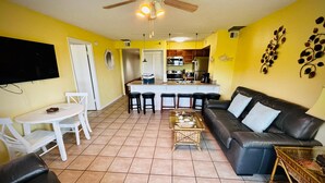 A living room with a black leather sofa, a white table, and a kitchen in the background. - Family-Friendly 1BR w/ Partial Ocean View & Pool (Tavernier)