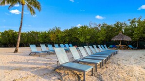 A beach with rows of blue lounge chairs and a thatched umbrella. - Family-Friendly 1BR w/ Partial Ocean View & Pool (Tavernier)