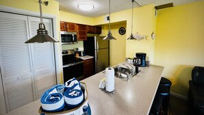 A compact kitchen with a microwave, stove, refrigerator, and a coffee maker. There are wooden cabinets and a sink. - Family-Friendly 1BR w/ Partial Ocean View & Pool (Tavernier)