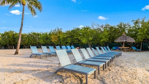 A beach with rows of blue lounge chairs and a thatched umbrella. - Key Largo 1BR - Ocean View, Near Founders Park (Tavernier)