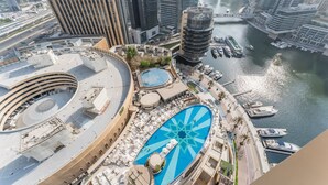 A high-rise hotel with a large circular pool, a marina with boats, and a view of the city skyline.